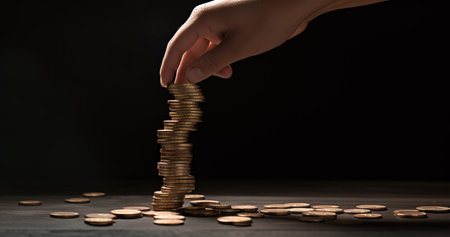 Female hand putting coin into stack of coins on black background, closeupの素材