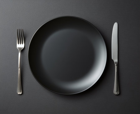 Empty black plate, knife and fork on black background, top viewの素材
