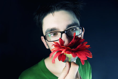 young guy with a red flower on a black backgroundの写真素材