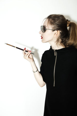 Young stylish woman wearing sunglasses with a cigarette holder on the light backgroundの写真素材