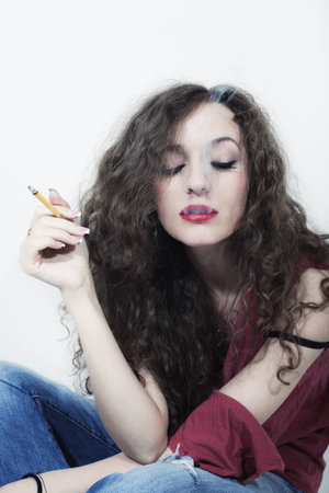 Young beautiful curly long-haired brunette woman with cigarette isolated on white backgroundの写真素材
