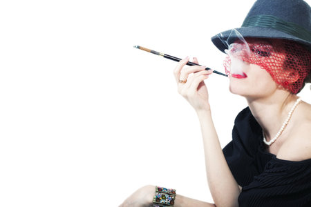 Young beautiful woman with cigarette in mouthpiece in  hat with veil on light background
