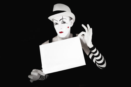 Funny mime in striped gloves and hat, holding a white  blank on a black backgroundの写真素材