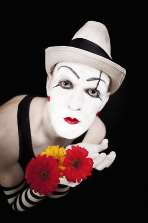 Funny mime in white hat with bouquet of red gerberas on black backgroundの写真素材