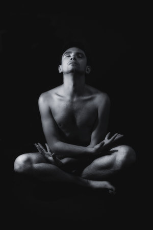 Meditation young naked man on a black backgroundの写真素材