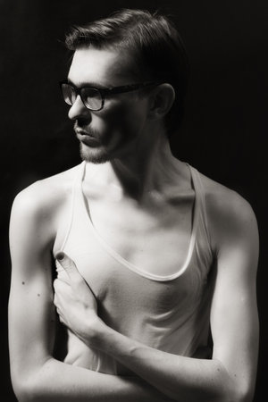 handsome young adult man in glasses and t-shirt on a black backgroundの写真素材