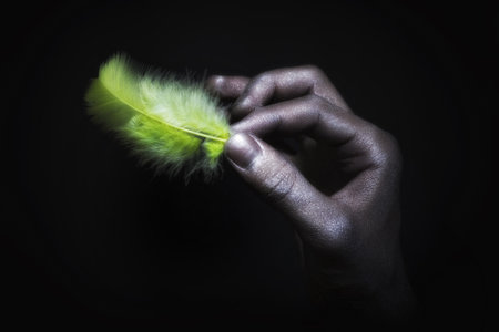 male hands in silver paint holding light green featherの写真素材