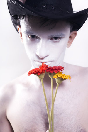 young man in black cowboy hat with white makeup on his face and bouquet of flowers on white backgroundの写真素材