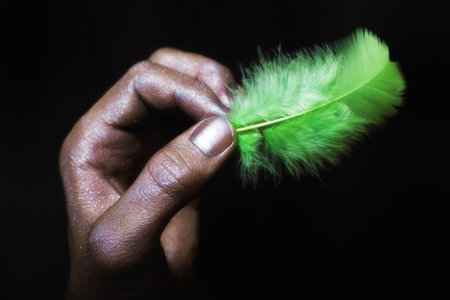 male hands in silver paint holding light green feather