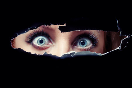 Women's blue eyes spying through a holeの写真素材