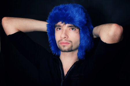 Studio portrait of a young Caucasian man in a blue winter hat on a black backgroundの写真素材