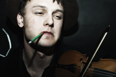 young handsome guy in hat with cigarette, playing the violinの写真素材