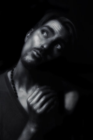 monochrome portrait of young attractive man with a silvery makeup on her face and hands against a...