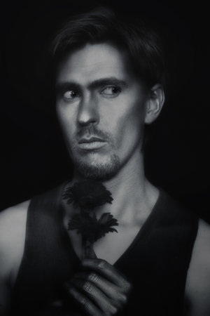 Portrait of young man with silvery makeup, holding red flowersの写真素材