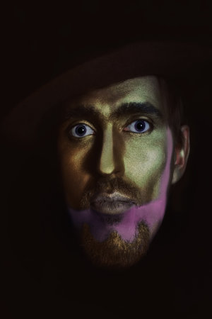 portrait of young attractive man in hat with bronze makeup on her face on black backgroundの写真素材