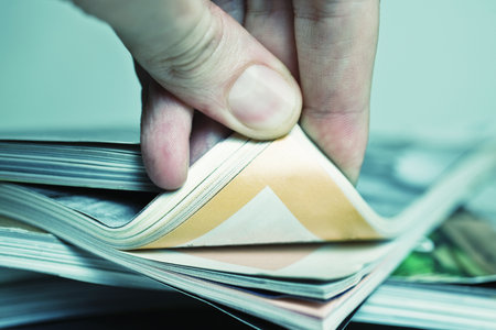 Man's hand turned over a stack of magazines closeup