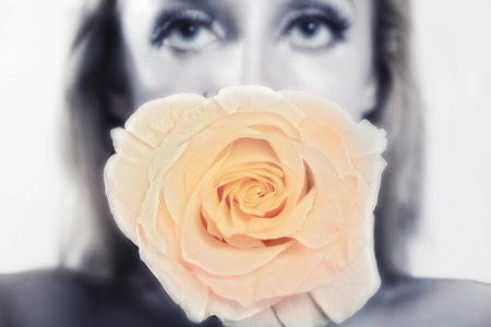 Young woman's face with silver makeup, holding a pink rose in her mouthの写真素材