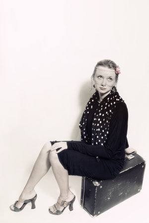 Young beautiful woman in retro style sitting on an old suitcase