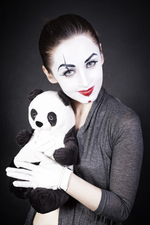 A woman mime with a toy panda on a black backgroundの写真素材