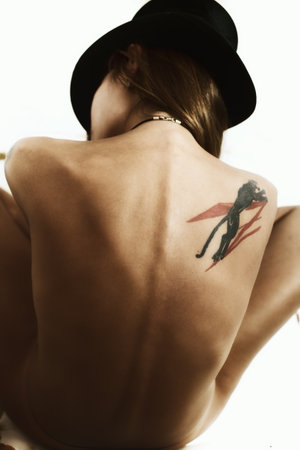 Back of naked suntanned young woman dressed in a black hatの写真素材