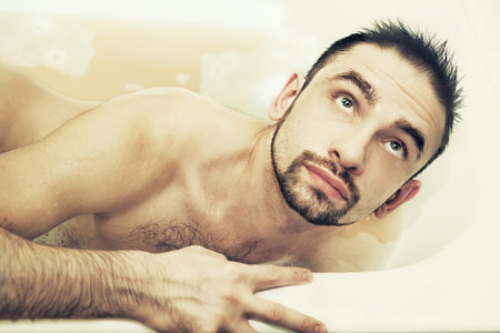 Beautiful naked young man lying in a bathtubの写真素材