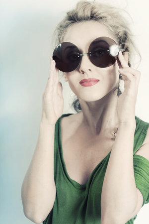 Portrait of young beautiful woman in the round sunglasses on light backgroundの写真素材