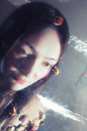 Face of girl with dry roses behind wet glass