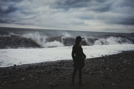 Woman dressed in a black coat on the beach during a stormの写真素材