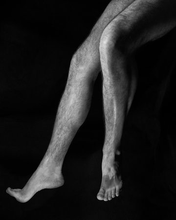 Beautiful, muscular, bare male feet on a black background. Classic high-contrast art photoの写真素材