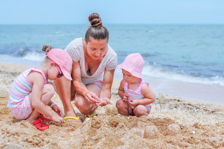 Little baby girl with mother and little sister on beachの写真素材