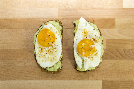 Healthy avocado toast and fried egg on whole grain bread on wooden background for breakfastの写真素材