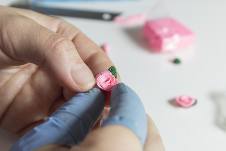 Women hands making floral jewelry from polymer clay, artist makes handmade pink rose earrings with green leaf. Workshop, clay modeling, art hobby. Handmade working. Withe backgroundの写真素材