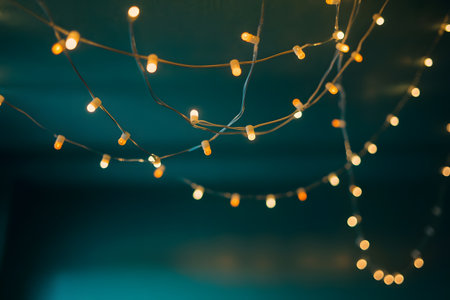 Softly glowing warm string lights illuminate a dark teal background, creating a festive and cozy ambiance for celebrationsの素材