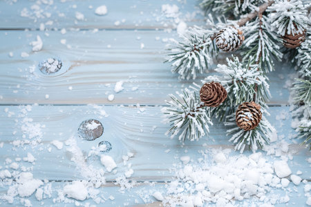 Snowy fir branches and pine cones on a light blue wooden background, perfect for winter, christmas, and holiday themesの素材