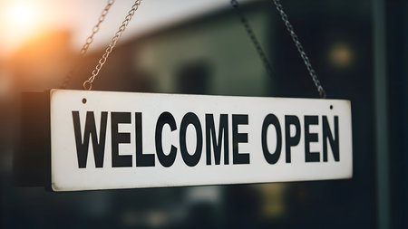 Welcome open" sign hanging on a glass door with a warm sun flare, indicating a business is ready for customers inside.の素材