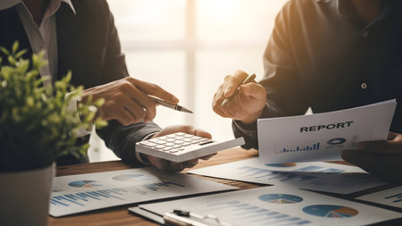 Business professionals collaborating over financial documents and graphs in a bright modern office settingの素材