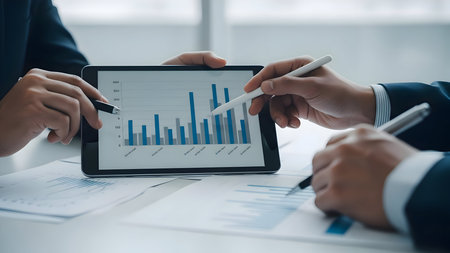 Business professionals collaborating over data analysis on a digital tablet in an officeの素材