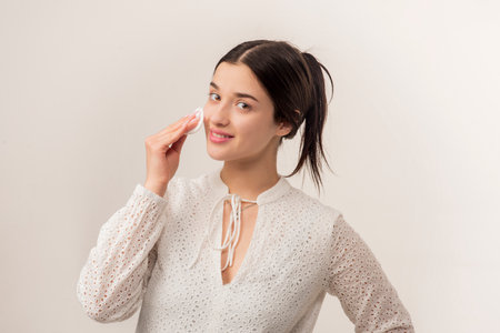 Beautiful young woman with cotton pad removing makeup. Skin care. Portrait of girl cleaning face with cotton pad. Beauty background. Face toner and cotton pad.の写真素材