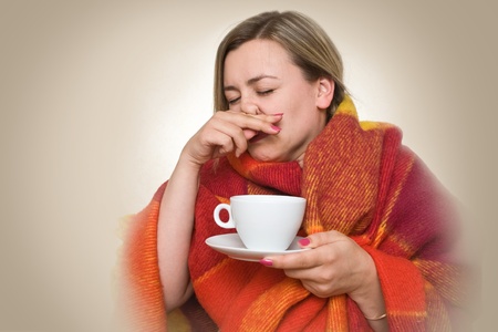 A young woman caught a cold, wrapped in a blanket and something hot drink from a cup.の写真素材
