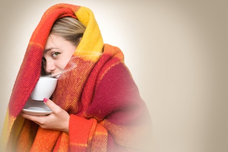 A young woman caught a cold, wrapped in a blanket and something hot drink from a cup.