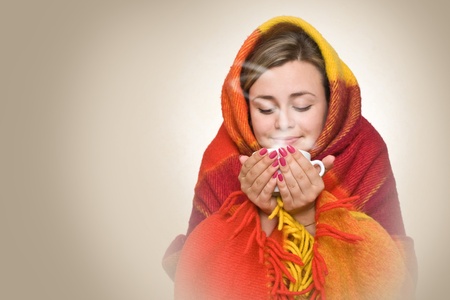 A young woman caught a cold, wrapped in a blanket and something hot drink from a cup.の写真素材