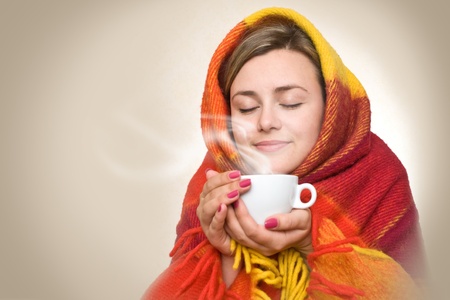 A young woman caught a cold, wrapped in a blanket and something hot drink from a cup.の写真素材