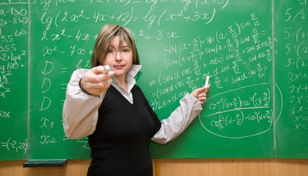 Happy teacher with text book gesturing and asking questions in school classroomの写真素材