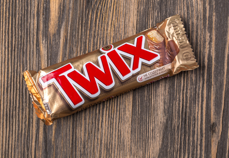 Chisinau, Moldova - August, 28, 2016. Twix wrapper on wooden background. Twix is a chocolate bar made by Mars, Inc., consisting of biscuit applied with caramel and milk chocolate.のeditorial素材