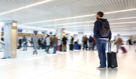 man stay with suitcase in modern airport terminal. Travelling guy wearing smart casual style clothes...