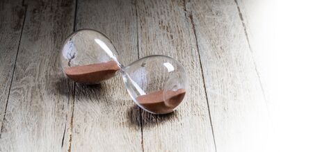 Glass hourglass lying on wooden background symbolize the stopped timeの写真素材