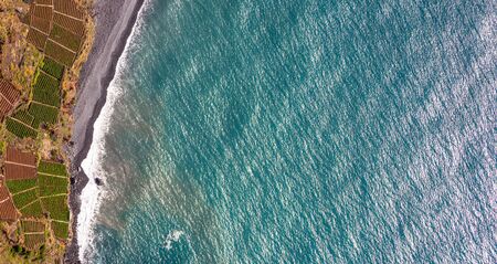Aerial landscape by the blue Atlantic ocean. Stone beach and adjacent fields on the southern coast of Madeira Island, Portugal.の写真素材