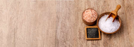 Mix of different salt types on wooden background with copy space. Sea salts, black and pink Himalayan salt crystals, collection of different types of salt.の写真素材