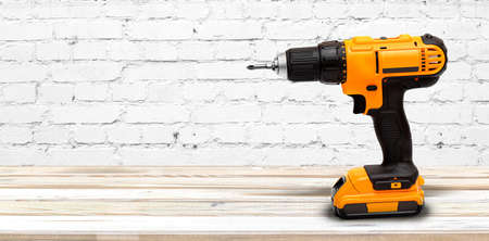 Yellow electric cordless screwdriver drill on white wooden background, professional home repair...