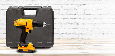 Yellow electric cordless screwdriver drill with box on white wooden background, professional home repair tool. Image with copy spaceの写真素材